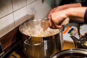 hand kock använder sig av trä- Flipper blandning ris med potatis i pott foto