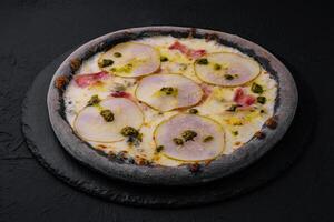 svart pizza med päron, ost och skinka foto