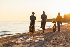 jord dag. volontärer aktivister team samlar sopor rengöring av strand kust zon. kvinna mannens med skräp i sopor väska på hav Strand. miljö- bevarande kust zon rengöring foto