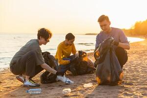 jord dag. volontärer aktivister team samlar sopor rengöring av strand kust zon. grupp av människor sätter plast skräp i sopor påsar på hav Strand. miljö- bevarande foto