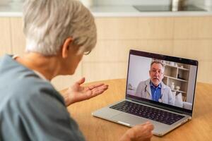 senior man läkare expert- granskning äldre senior kvinna uppkopplad. gammal kvinna lady patient och läkare prata på video ring upp ha samråd med bärbar dator. medicin sjukvård medicinsk kolla upp. uppkopplad läkare foto