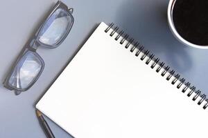 anteckningsblock med kaffe kopp, läsning glasögon och en penna på en skrivbord. kopia Plats. foto