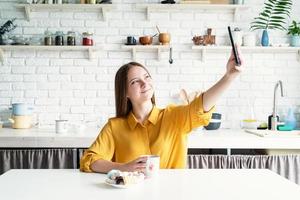 ung kvinna som tar en selfie medan hon tar en kopp morgonkaffe i köket foto