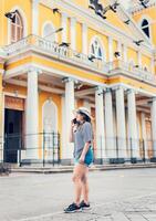 kvinna turist talande på cell telefon i de fyrkant. granada, nicaragua. Lycklig resa kvinna kallelse på de telefon i på de gata foto