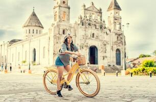 livsstil av en Lycklig flicka i hatt på cykel på de gata. granada, nicaragua. Lycklig flicka i hatt ridning en cykel på solnedgång. turism och resa begrepp foto