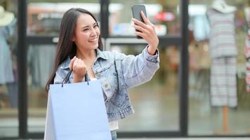 asian shopper använder en smartphone för att ta en selfie. hon stod och höll i en påse.