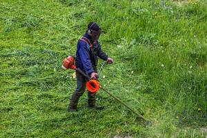 gräsklippare man med sträng trimmer trimning gräs på solig dag foto