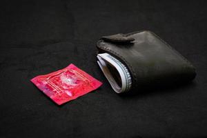 närbild svart läder plånbok med en röd kondom på den svarta bakgrunden foto