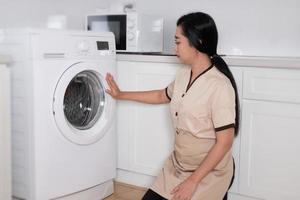 ung vacker asiatpiga som laddar tvättmaskinens kläder på hotellrummet foto
