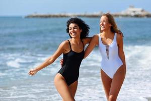 två unga kvinnor med vackra kroppar i baddräkt på en tropisk strand foto