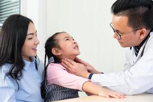 asiatisk läkare palpera livmoderhals lymfkörtlar i nacken på ung flicka som har ont i halsen och besök på sjukhuskliniken. hälsovård och medicinsk koncept foto