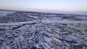 antenn se av en stor stad med byggnad tak täckt förbi snö. klämma. flygande ovan frysta stad och en flod. foto