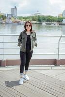 ung skön asiatisk kvinna bär jacka och svart jeans Framställ utomhus foto