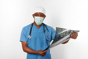 svart kirurg läkare man i blå täcka vit keps och kirurg mask innehar x stråle bild, vit bakgrund foto