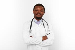 leende svart skäggig läkare man korsade vapen i vit täcka med stetoskop, vit bakgrund foto
