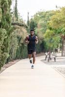 afrikansk amerikan sportsman i aktiva kläder joggning längs parkera under morgon- övning foto