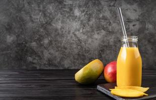 färsk mangoskaka i ett glas med ett drickshalm av metall dekorerat med skivor av mango framifrån på mörk träbakgrund foto