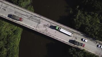 topp se av godkänd fordon på bro över flod. klämma. lastbilar och bilar kör över bro över brun flod. körning tvärs över bro på solig sommar dag foto