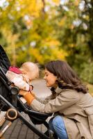 ung kvinna med söt bebis flicka i bebis sittvagn på de höst parkera foto