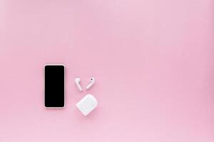 smartphone med trådlös hörlurar på rosa bakgrund foto