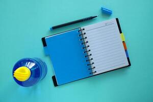 öppnad anteckningsbok med penna och vatten flaska på blå bakgrund foto