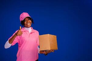 skön afrikansk kvinna kurir arbetstagare innehav en låda, gör en tummen upp gest foto