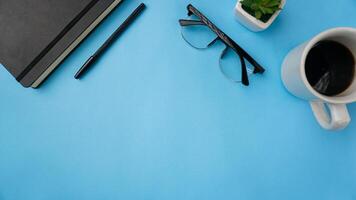 arbetsyta skrivbord med anteckningsböcker, pennor, glasögon, och kaffe på blå bakgrund foto