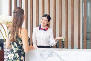 ung asiatisk kvinna receptionist Bakom de hotell disken delta till kvinna gäster. leende kvinna receptionist arbetssätt i en hotell foto