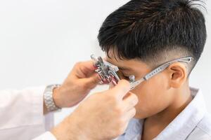 pojke håller på med öga testa kontroll undersökning med optiker i optisk affär, optiker håller på med syn testning för barn patient i klinik, indisk barn välja glasögon i optik Lagra foto