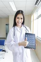 porträtt av smart kvinnlig läkare som håller tablett för att visa röntgenbild och står vid receptionen på sjukhuset. foto