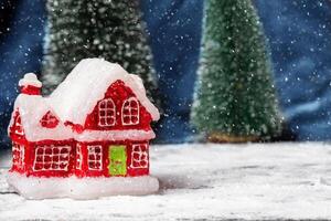 röd jul leksak hus mot de bakgrund av gran träd och flygande snöflingor. jul barns kort. foto