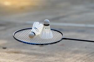 vit fjäderboll 2 placerad sida förbi sida på en badminton racket med en cement bakgrund.mjuk och selektiv fokus foto