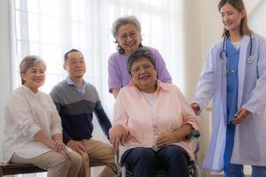 asiatisk ung sjuksköterska Stöd par senior äldre kvinna i en rullstol. äldre mogna och en grupp av senior vänner levande i de sjukhus. umgänge av pensionerad människor. foto