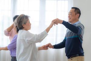 asiatisk äldre manlig och honor människor dansa med deras partners på en dans golv i levande Plats. Lycklig äldre par utför skaffa sig träning. glad sorglös pensionerad senior vänner njuter avslappning foto