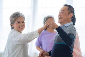 asiatisk äldre manlig och honor människor dansa med deras partners på en dans golv i levande Plats. Lycklig äldre par utför skaffa sig träning. glad sorglös pensionerad senior vänner njuter avslappning foto