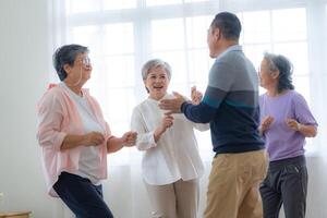 asiatisk äldre manlig och honor människor dansa med deras partners på en dans golv i levande Plats. Lycklig äldre par utför skaffa sig träning. glad sorglös pensionerad senior vänner njuter avslappning foto