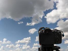 svart professionell digital kamera på en stativ spetsig på blå himmel med vit moln foto