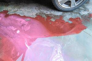 pöl av rosa kylmedel och brun teknisk vätskor på de betong golv nära bil foto