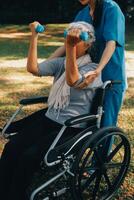 ung sjuksköterska eller fysioterapeut i scrubs portion en Lycklig pensionerad gammal kvinna do kondition övningar med ljus vikt hantlar på Hem. begrepp av fysioterapi för seniors foto