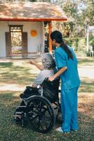 ung asiatisk vård hjälpare med Asien äldre kvinna på rullstol koppla av tillsammans parkera utomhus till hjälp och uppmuntra och resten din sinne med grön natur. hjälp Stöd själv till lära sig till promenad. rollator foto