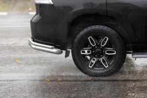 regn vatten stänk flöden från hjul av svart bil den där rör på sig snabb på asfalt väg foto