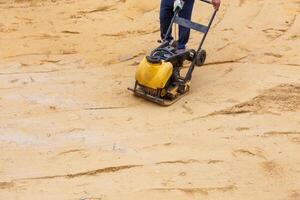 arbetstagare använder sig av vibrerande tallrik komprimator för kompaktering sand under väg konstruktion. foto