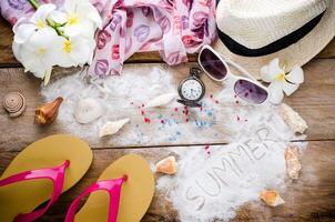 hav resa Tillbehör en hatt, solglasögon, sandaler. placerad på trä- med ord sommar på sand. foto