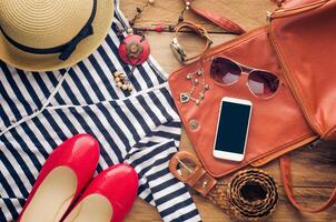 Tillbehör för Tonårs flicka på henne semester. sugrör hatt, eleganta solglasögon, brun läder väska, röd skor och kostym på trä- golv. foto