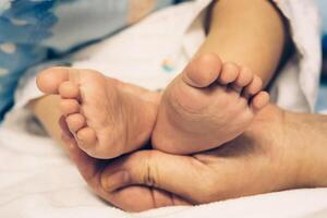 de händer av de mor håll de bebis fötter med kärlek och omtänksam. foto