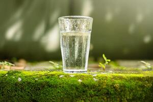 värld vatten dag begrepp. vatten dryck glas. friskhet och kall. omringad förbi grön mossa och naturlig morgon- solljus miljö foto