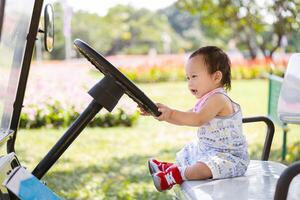 glad bebis pojke låtsas till kör golf vagn, småbarn skrattar med glädje medan låtsas till styra golf vagn, med skön blomma trädgård i full blomma som hans inbillade destination. barn åldrig 1 år foto