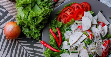 kryddad glas nudel sallad med vietnamese korv eras i en grå tallrik sätta på en trä- tabell och olika grönsaker. foto