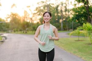 passa asiatisk ung kvinna joggning i parkera leende Lycklig löpning och njuter en friska utomhus- livsstil. kvinna joggare. kondition löpare flicka i offentlig parkera. friska livsstil och wellness varelse begrepp foto