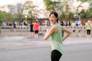 kvinna joggare. passa ung asiatisk kvinna med grön sportkläder aerobics dansa övning i parkera och njuter en friska utomhus. kondition löpare flicka i offentlig parkera. wellness varelse begrepp foto